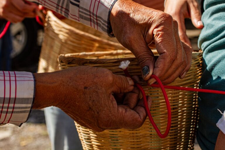 Hands weaving a basket with red cord outdoors